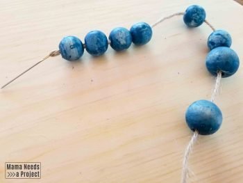 threading wooden beads onto jute with a sewing needle