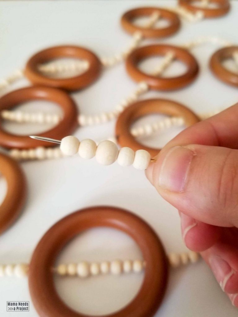 thread wood beads and rings onto string with an embroidery needle