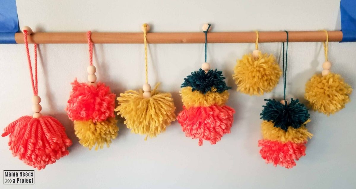 pom pom christmas ornaments hanging from a wooden dowel