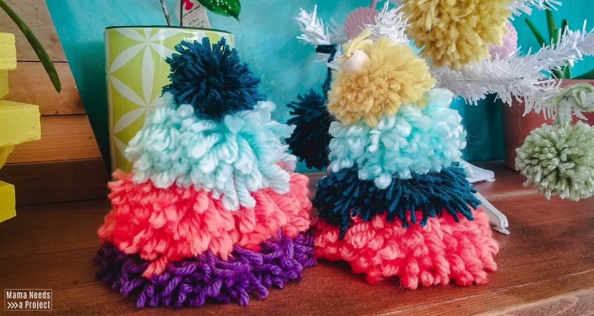 two colorful pom pom christmas trees in front front of a teal wall