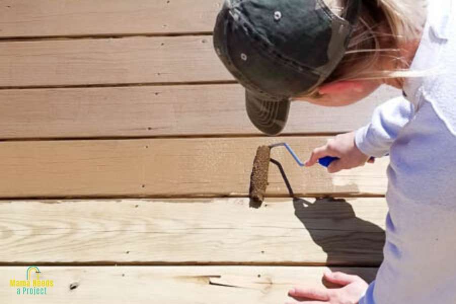 restaining a wood deck - woman staining wood deck with a roller