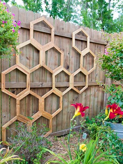 honeycomb garden trellis on fence with red flowers blooming in front