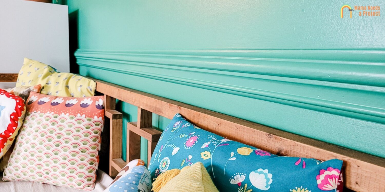 green painted trim on a green wall above a wood couch with colorful pillows