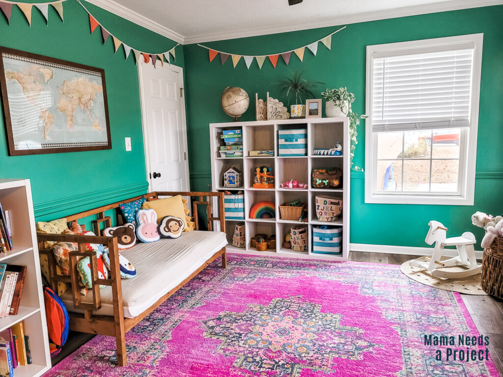 playroom with green walls and green painted chair rail trim, white shelves with toys, colorful wall decor and room decor, pink rug, colorful playroom