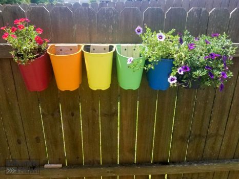 Upcycled plastic nursery pots mounted to fence with flower planted, rainbow colors